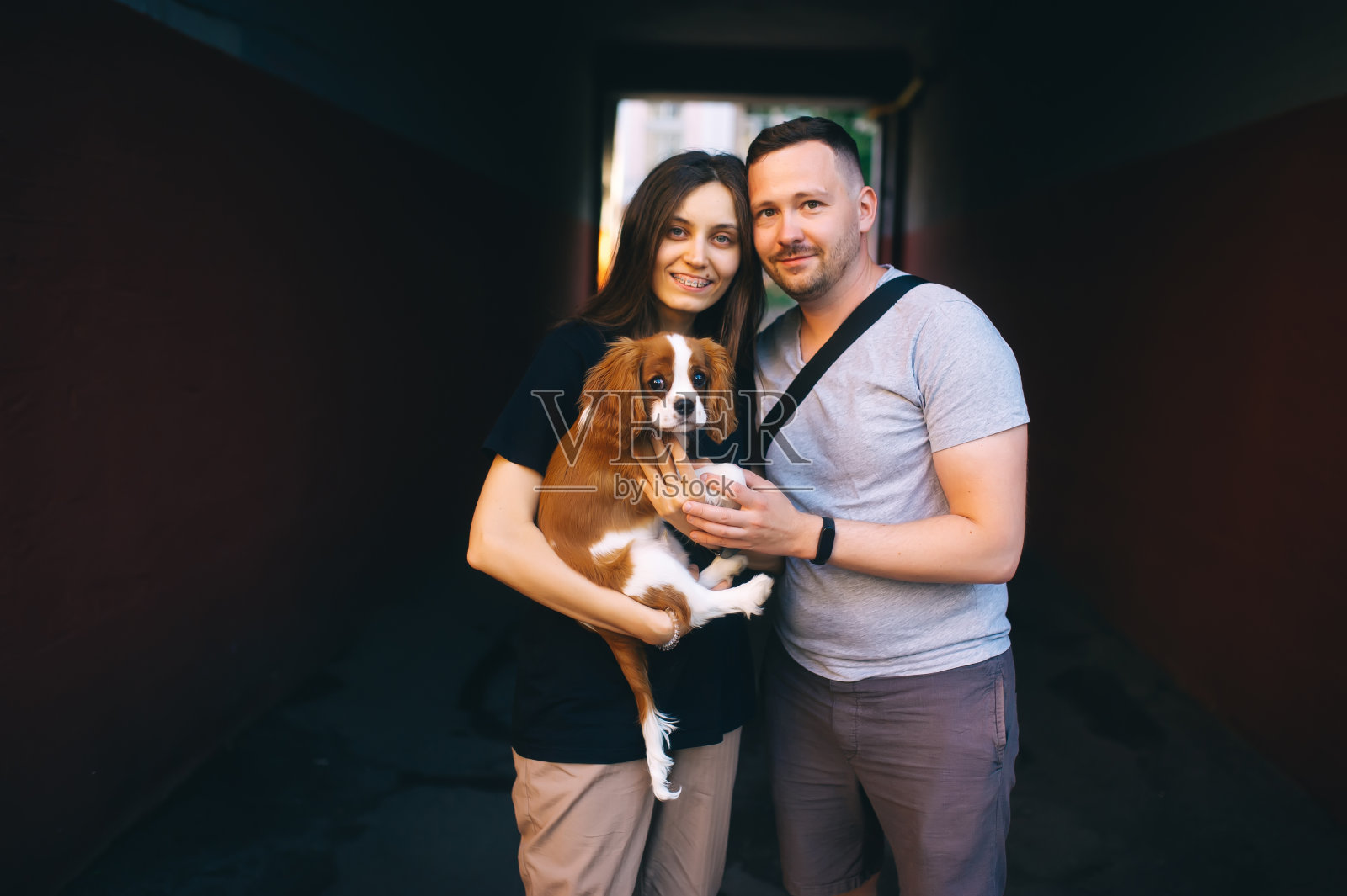 一对美丽幸福的夫妇对着镜头微笑,抱着她可爱的查尔斯王猎犬。照片摄影图片