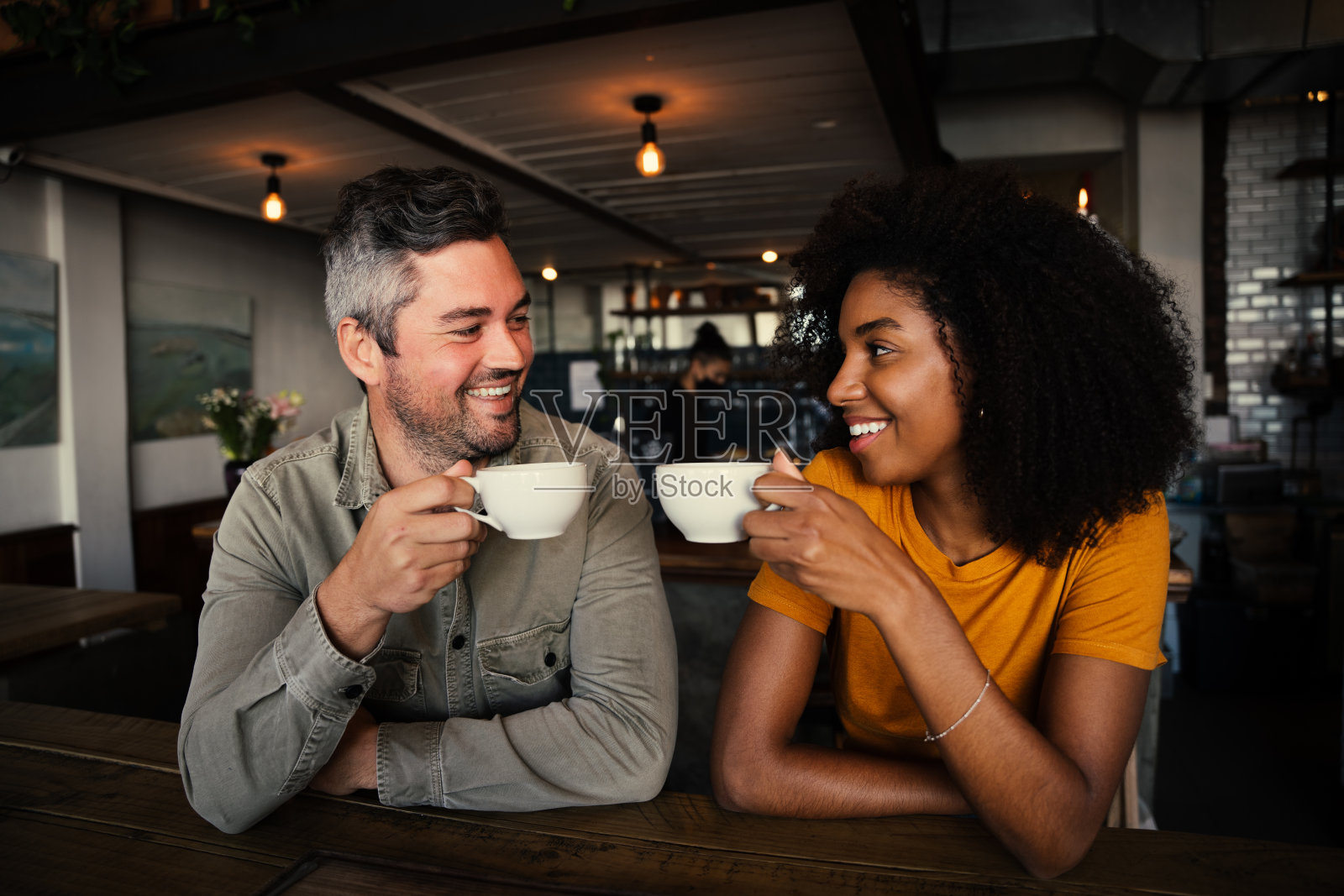 在时髦的咖啡店里,微笑的混血夫妇碰杯喝咖啡照片摄影图片