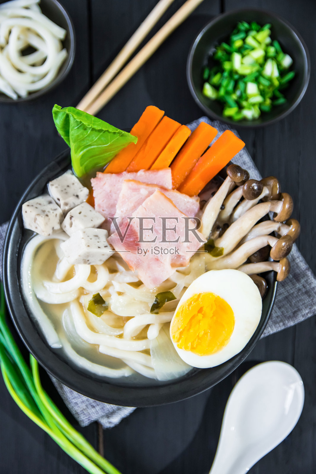 美味。亚洲自制面汤,猪肉培根拉面,豆腐,蘑菇蔬菜,和煮鸡蛋在黑碗背景,顶级照片摄影图片