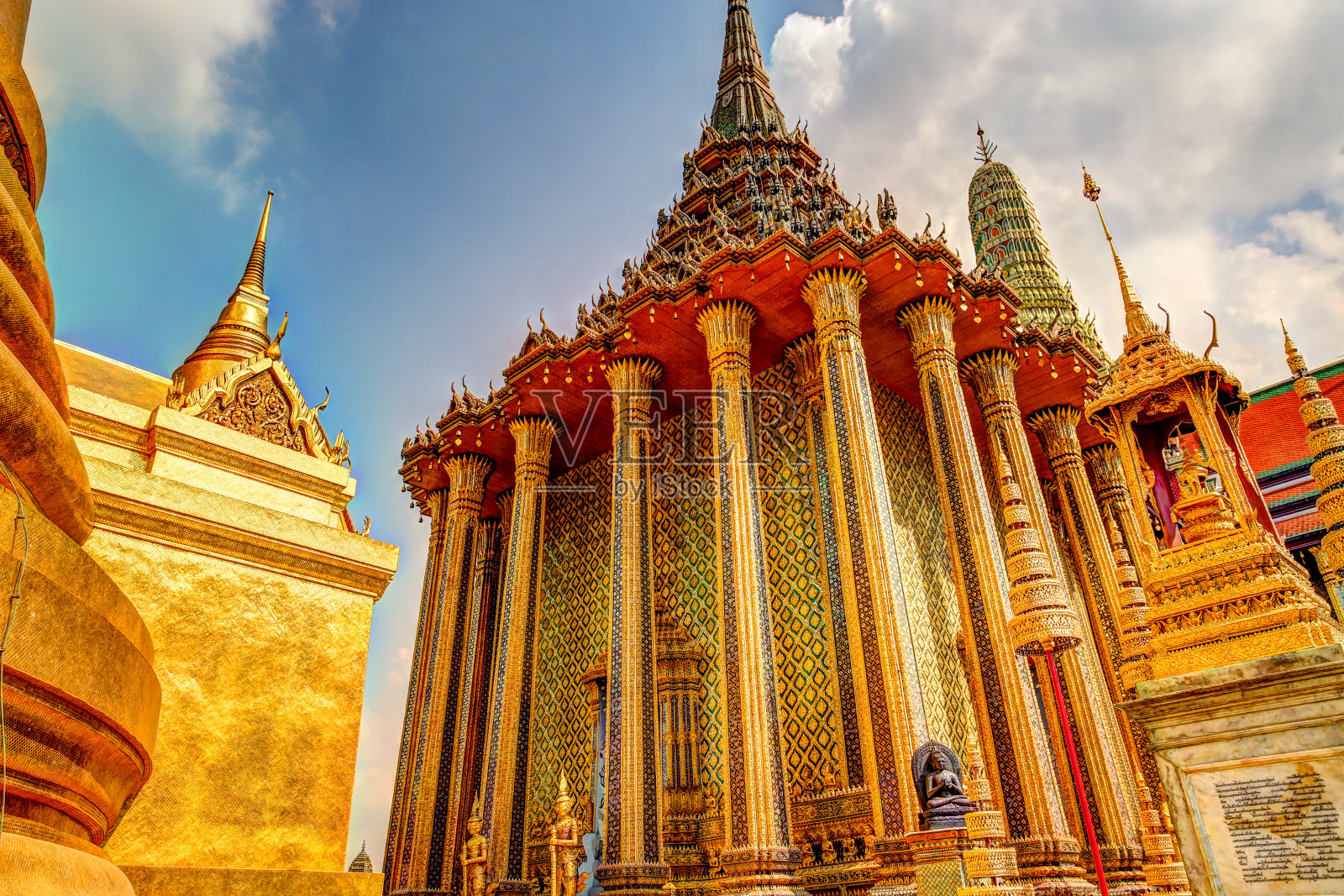 泰国曼谷大皇宫中雄伟的金柱和宝塔映衬着多云的天空照片摄影图片