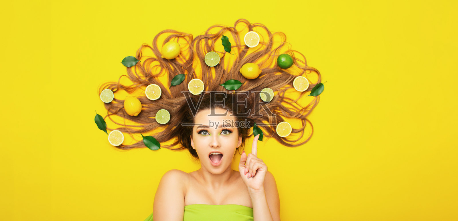 美丽的女孩躺在黄色的背景与柑桔水果在长头发,年轻女子举起大拇指有好主意照片摄影图片