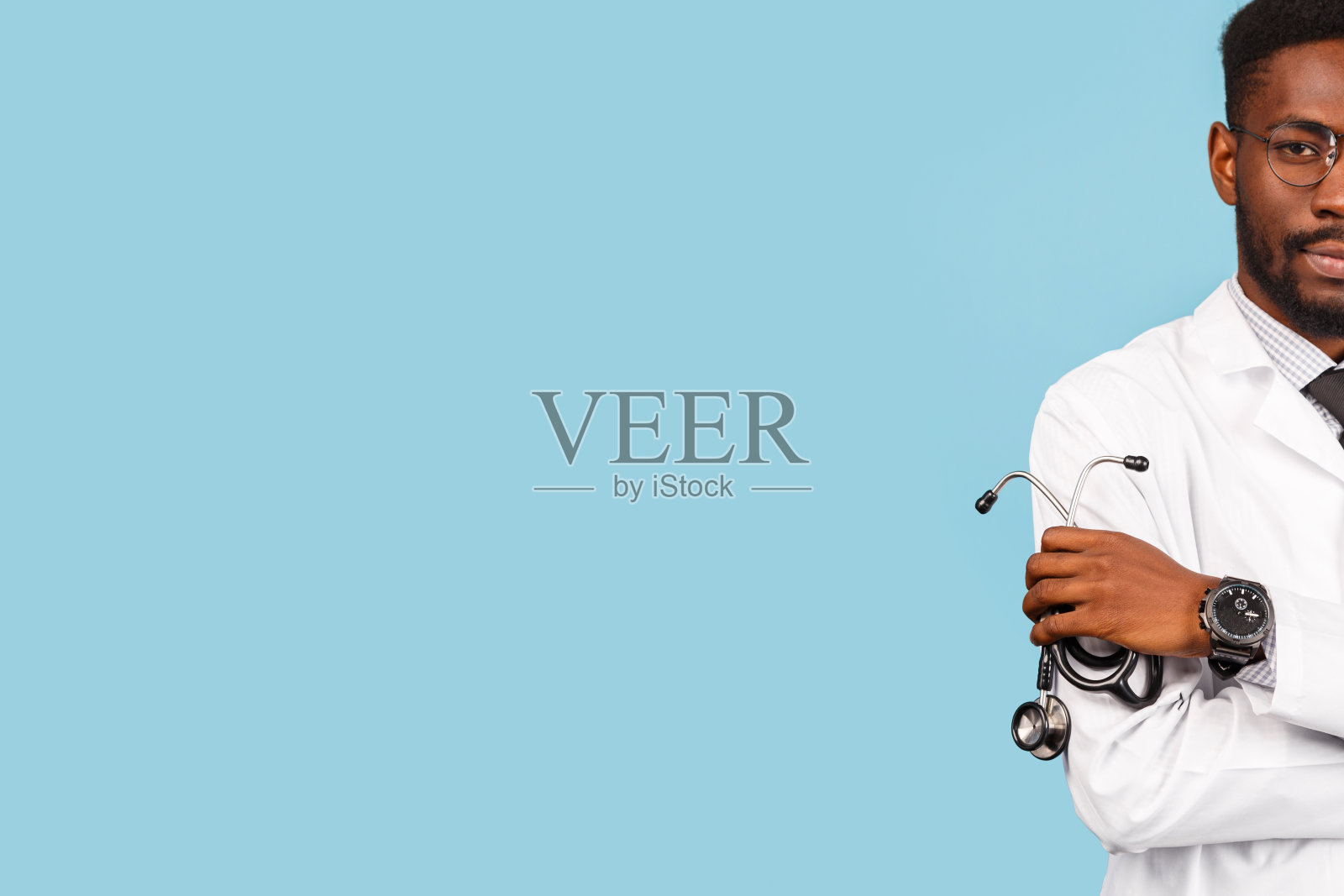 英俊的非裔美国男医生,带听诊器,双臂交叉,背景为蓝色。医学和医疗照片摄影图片