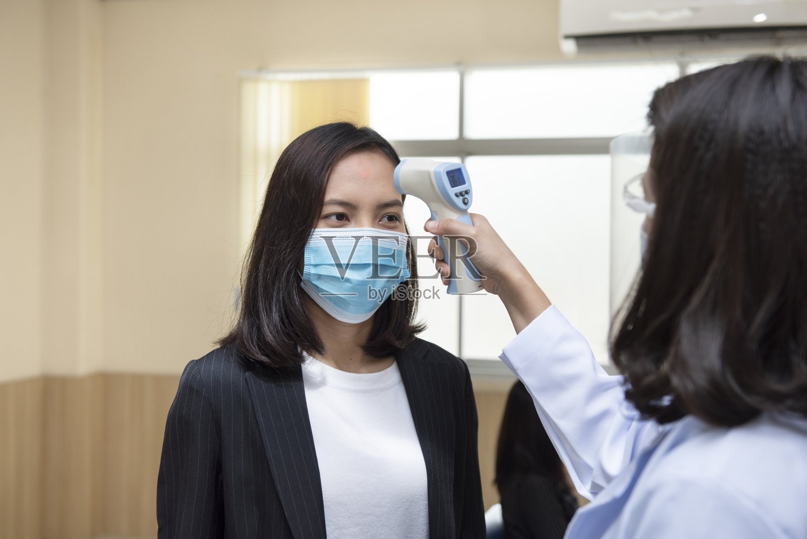 医生在医院用红外线额头体温计检查亚洲妇女的体温,看是否有病毒症状。照片摄影图片