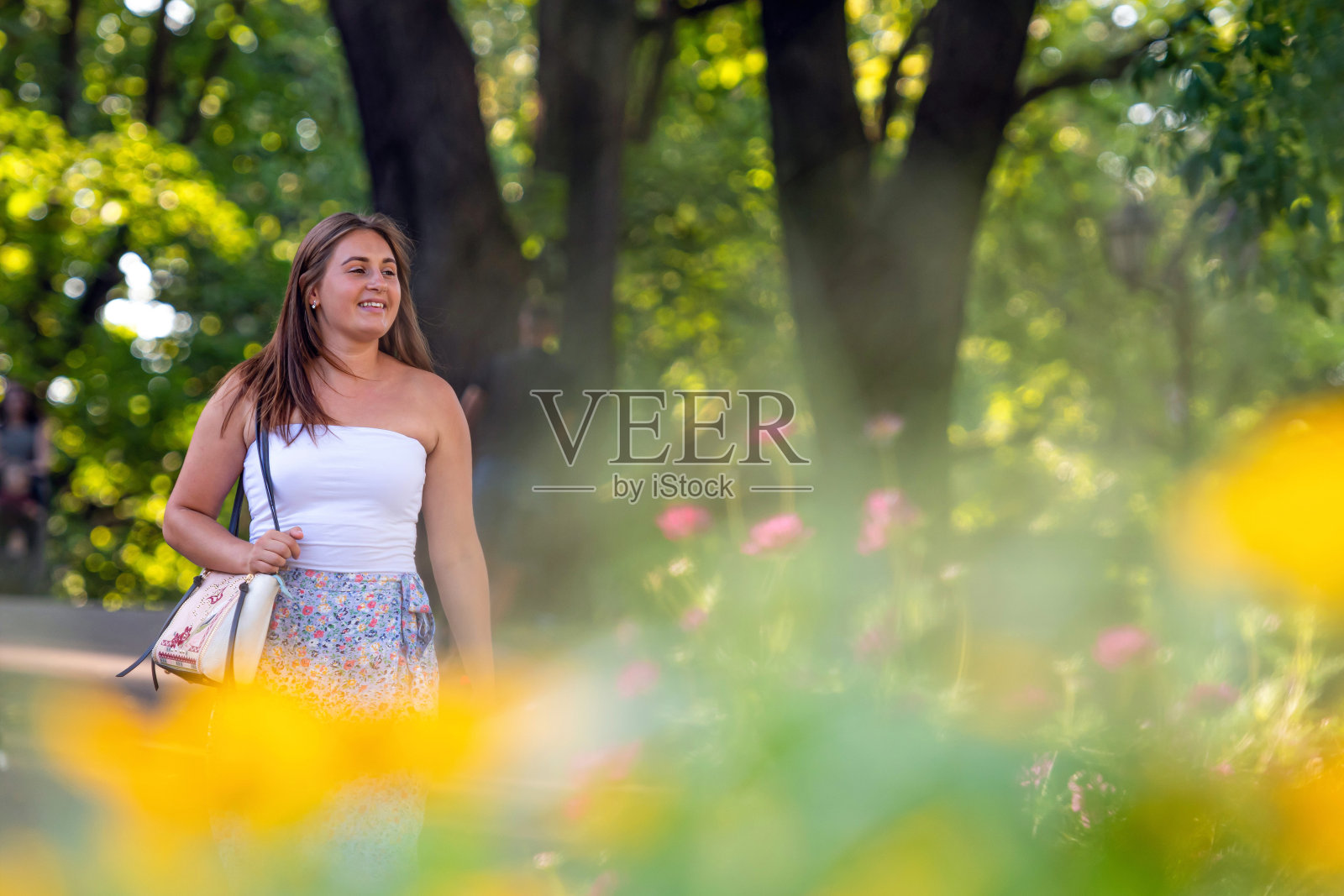 一个穿着浅色上衣和杂色裙子的年轻女子走过城市公园照片摄影图片