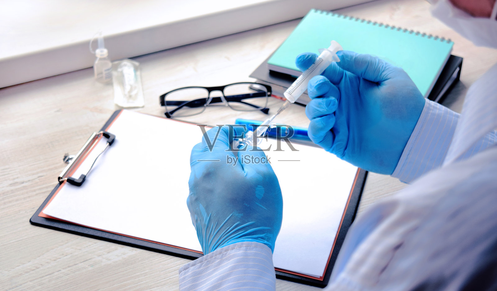 医生或药剂师坐在桌子上,手里拿着一个注射器。医疗保健的概念。接种疫苗。照片摄影图片