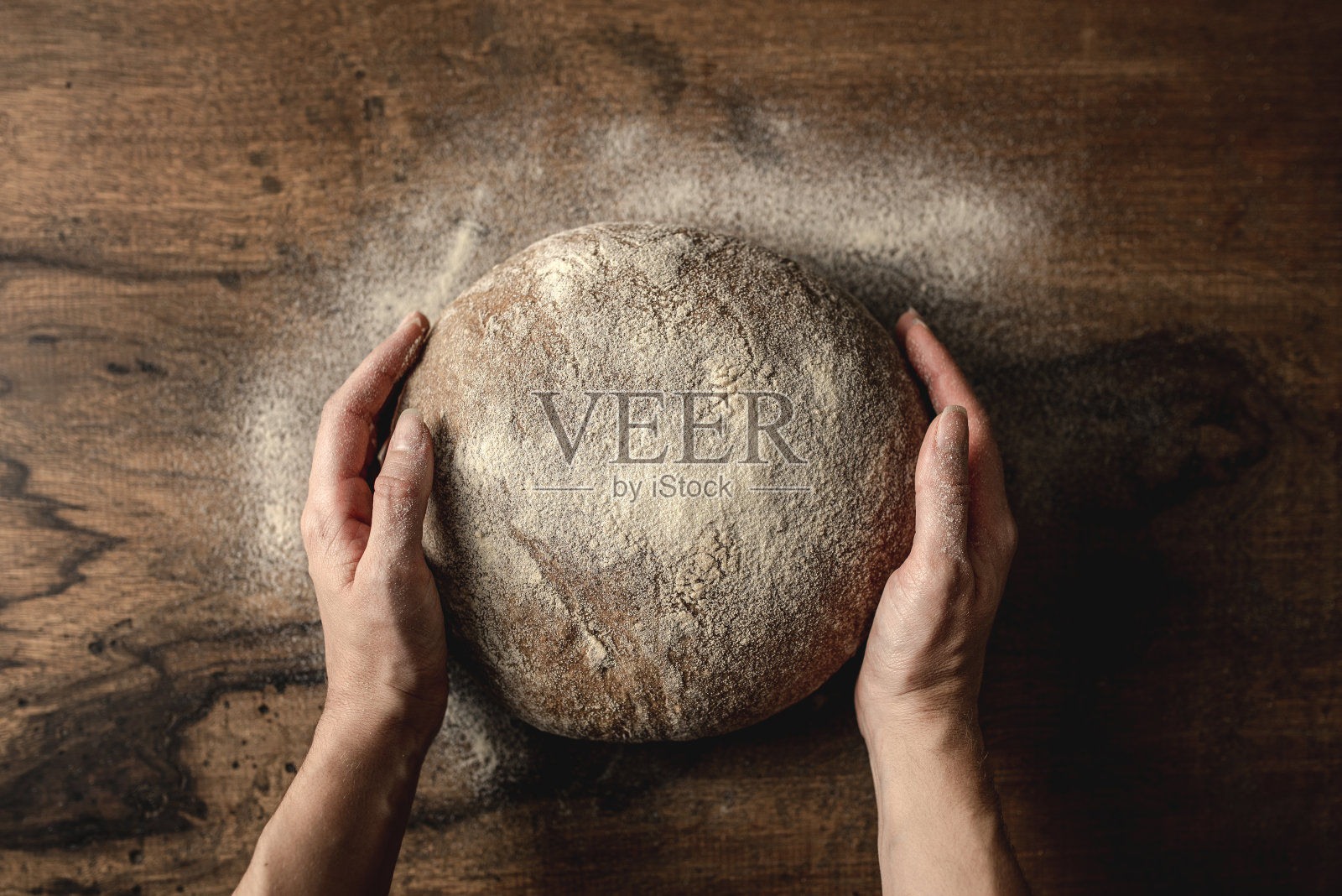 双手把黑麦面包放在木桌上。照片摄影图片