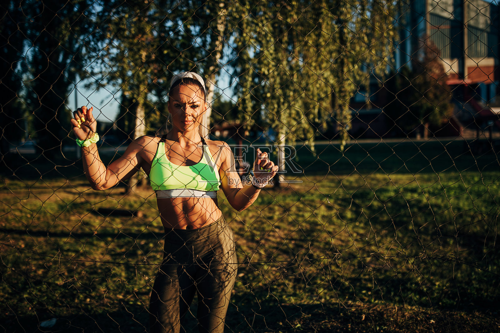 女运动员靠在铁丝网围栏周围的室外球场和看摄像机照片摄影图片