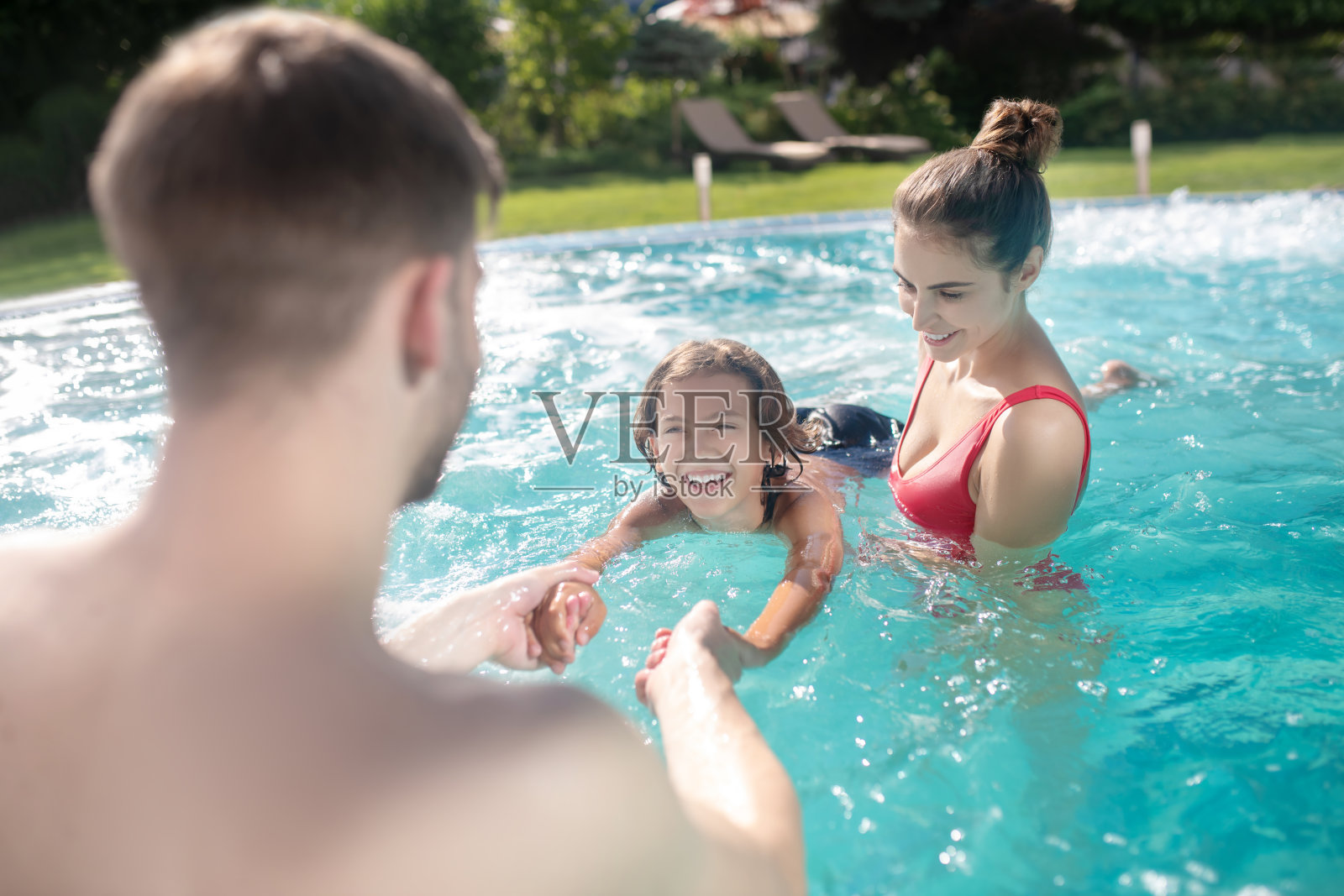 兴奋的父母在游泳池教他们的儿子游泳照片摄影图片