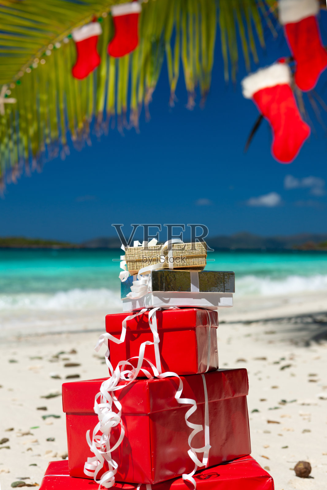 热带海滩上的一棵棕榈树,上面挂着圣诞装饰品、长筒袜和礼物照片摄影图片