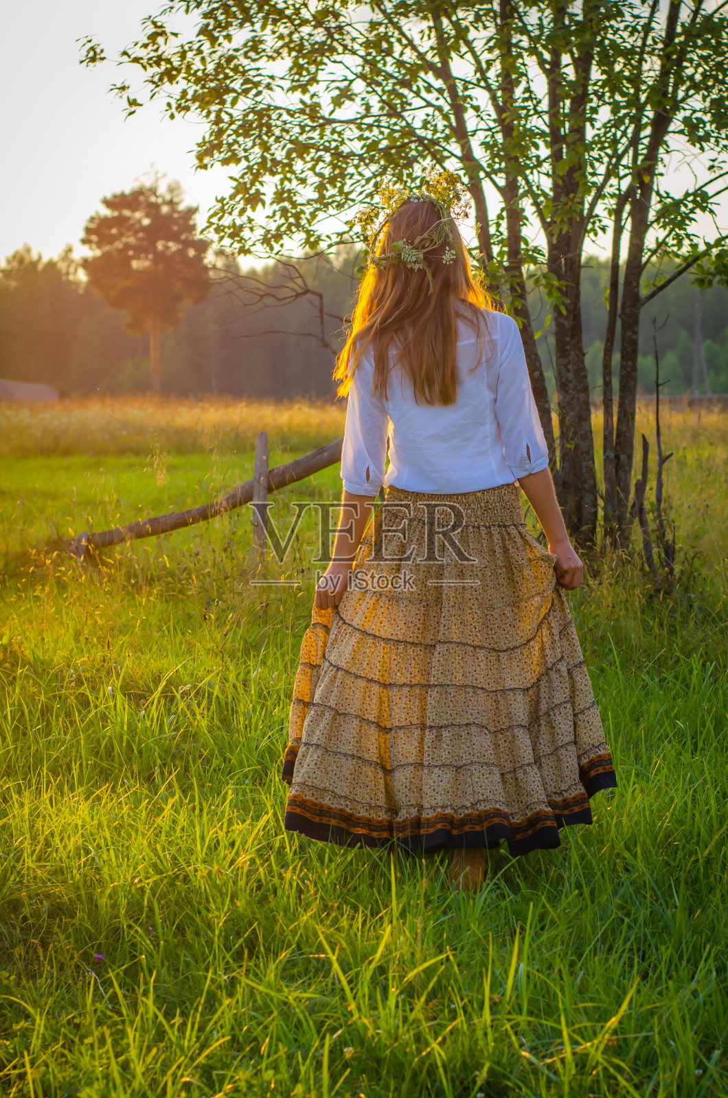美丽浪漫的女人,身穿白色衬衫和长裙,头上戴着花环,背景是夕阳下的乡村风景。夏天的概念。照片摄影图片