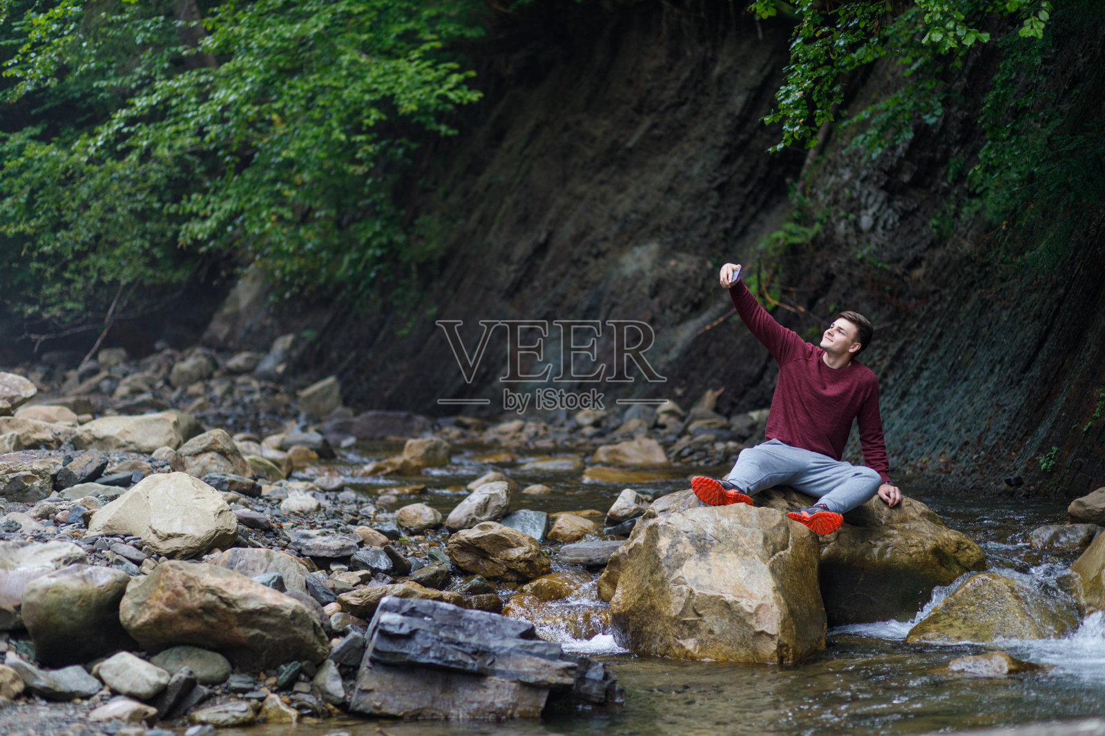 一个年轻人用手机在石头上拍自己的照片。照片摄影图片