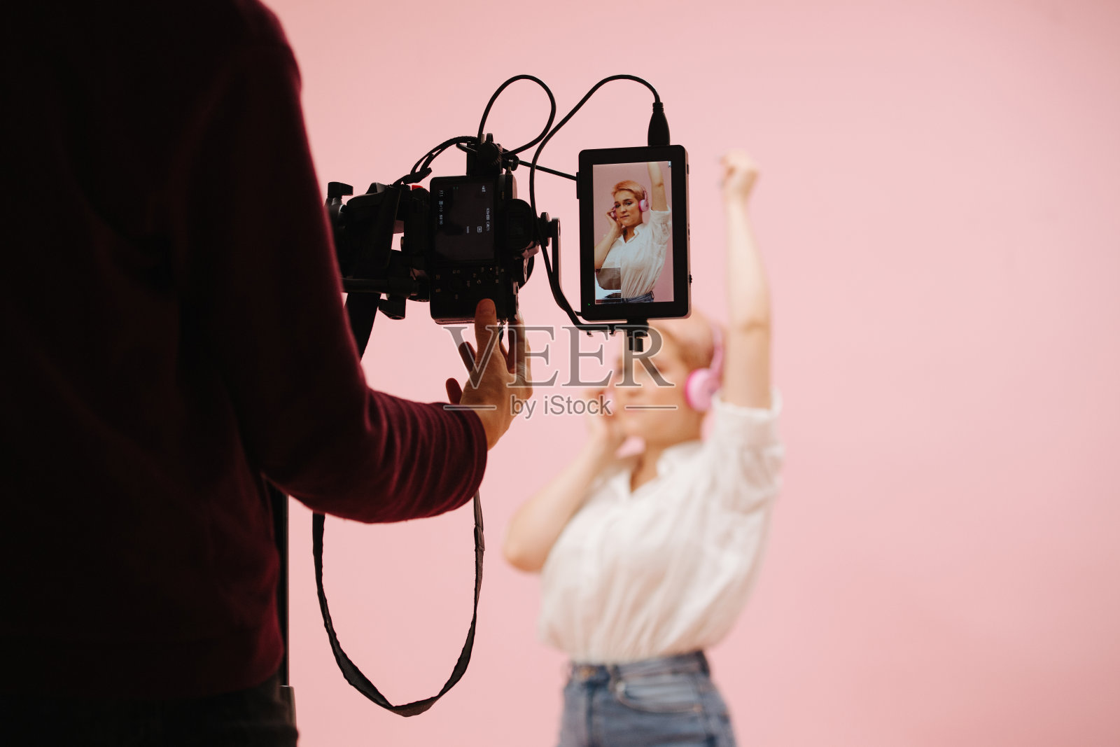 在现场监控器的帮助下拍摄年轻女子。她戴着耳机摆姿势。照片摄影图片