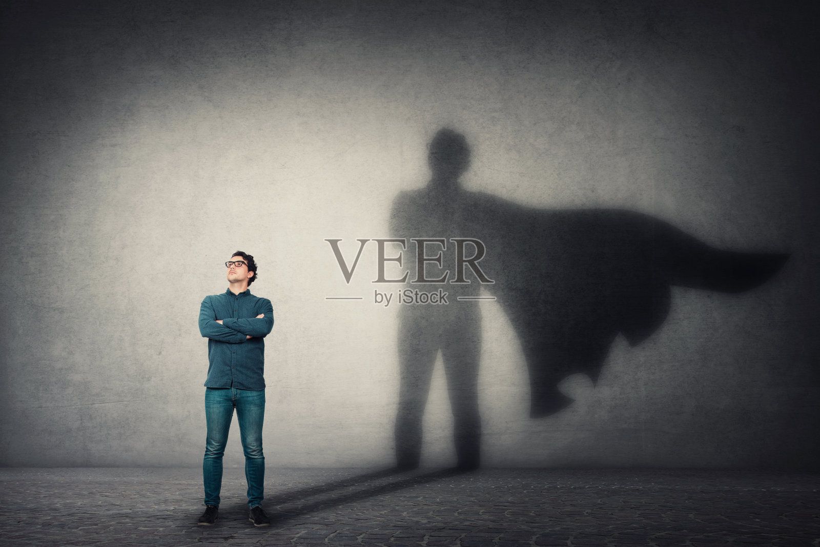 勇敢的人双臂交叉,看起来很自信,在墙上投下了一个有着斗篷阴影的超级英雄。野心和商业成功的概念。领导能力是英雄力量、激励和内在力量的象征。照片摄影图片