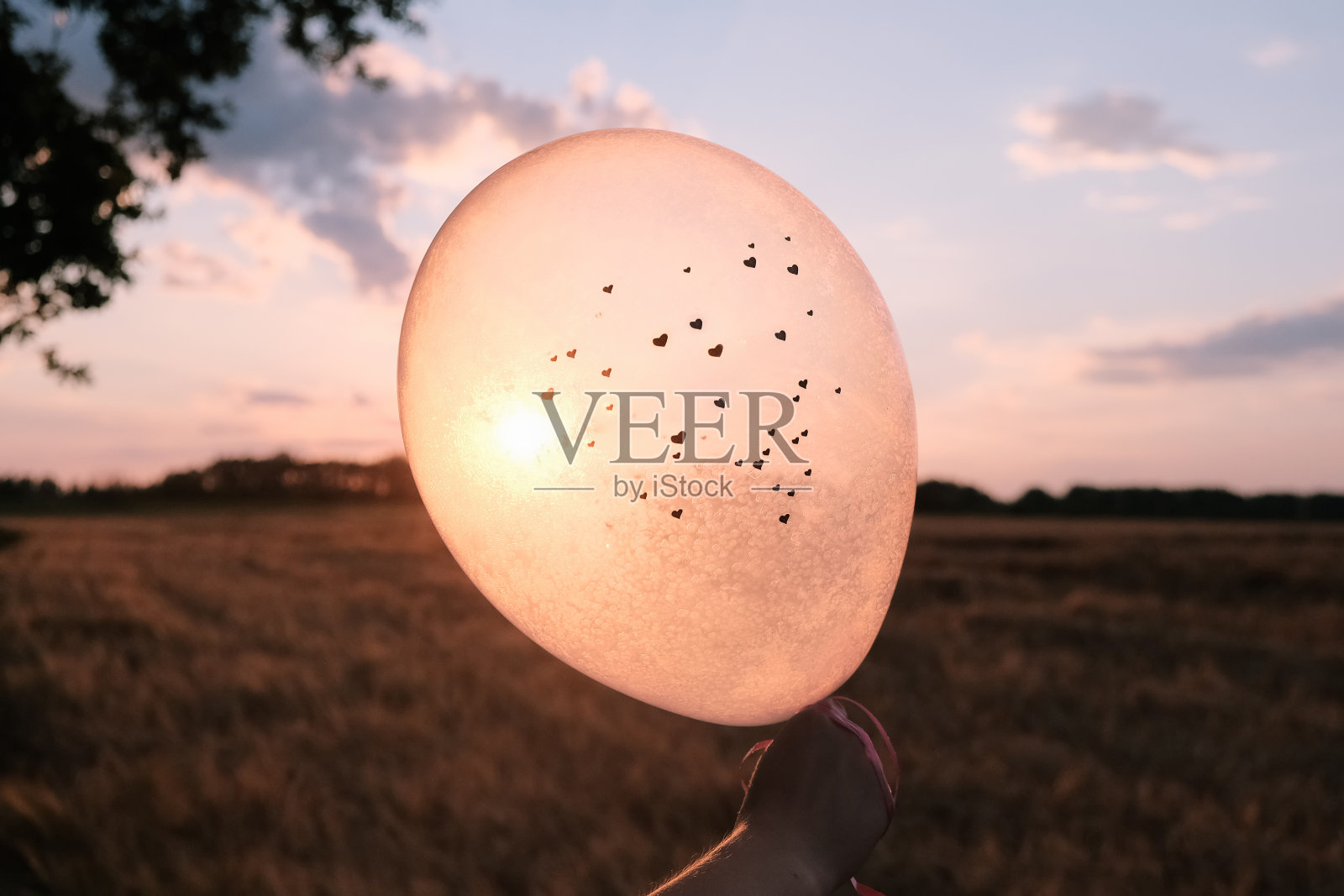 夕阳下紫色的天空中,女性手握心形气球的轮廓照片摄影图片