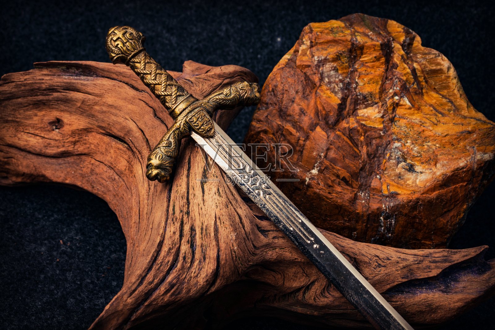 骑士的剑在一个古老的纹理木制浮木和棕色的粗糙的石头的背景照片摄影图片