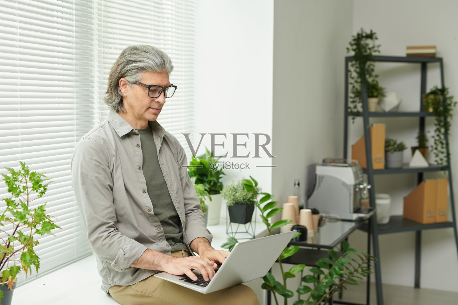 专注成熟的经理戴着眼镜坐在窗台上,带着盆栽,用笔记本电脑进行营销项目照片摄影图片