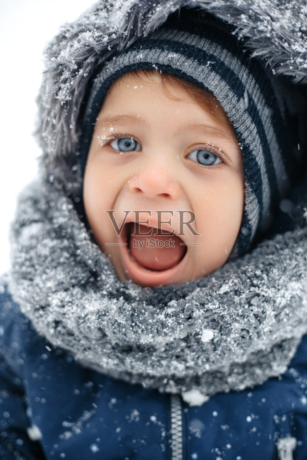 可爱的小男孩穿着温暖的白色雪衣,张着嘴笑。照片摄影图片