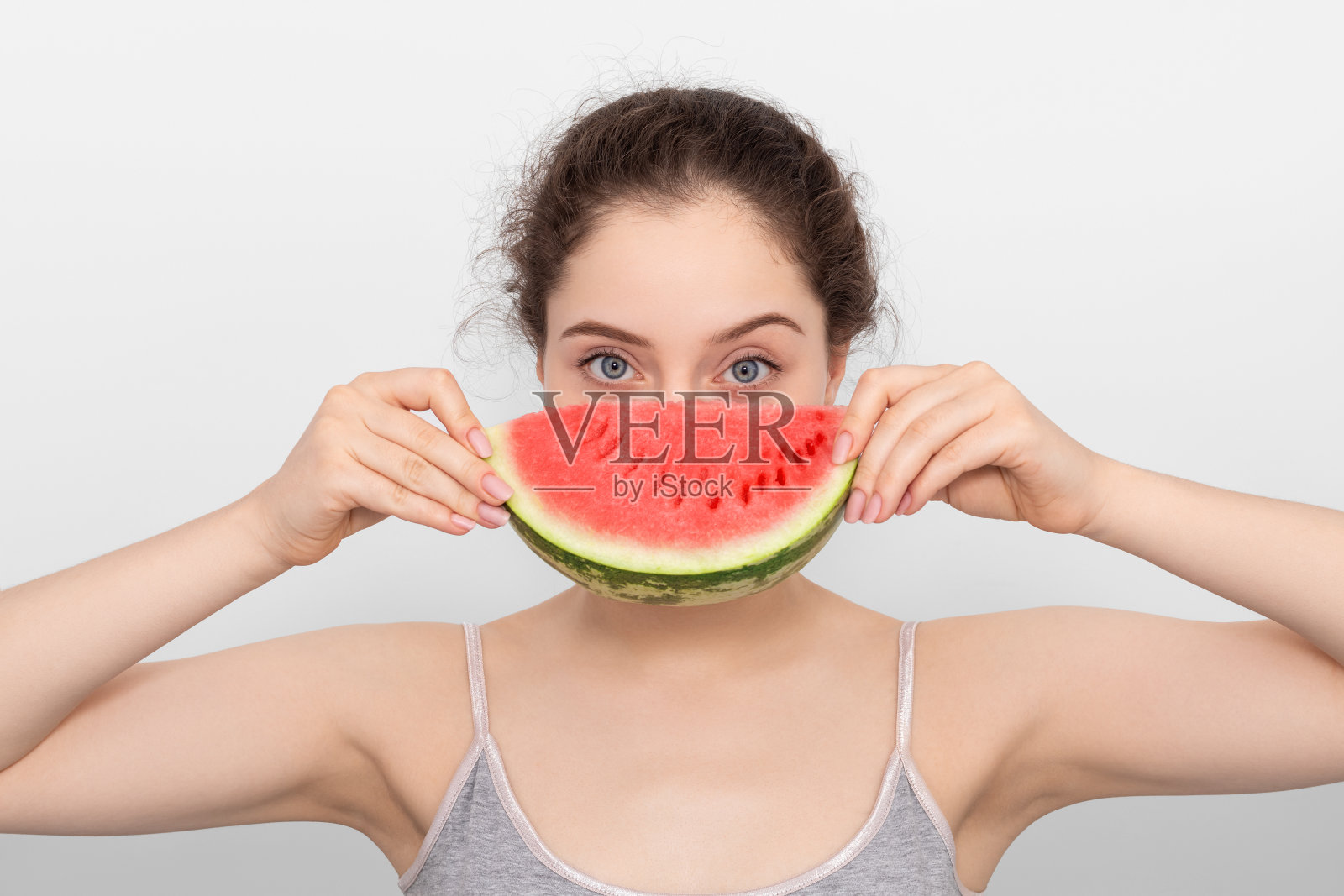 拿着西瓜的女孩,灰色背景上穿着灰色t恤。照片摄影图片