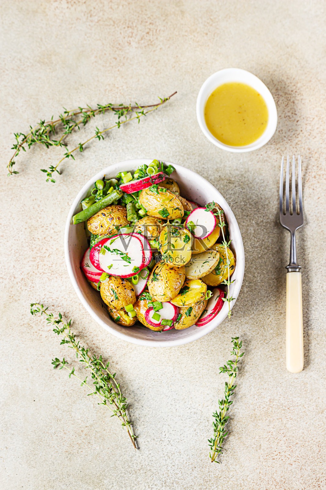 美味的热土豆沙拉与青豆,新鲜的萝卜和香草调味橄榄油和芥末酱,淡淡的混凝土背景。前视图。照片摄影图片