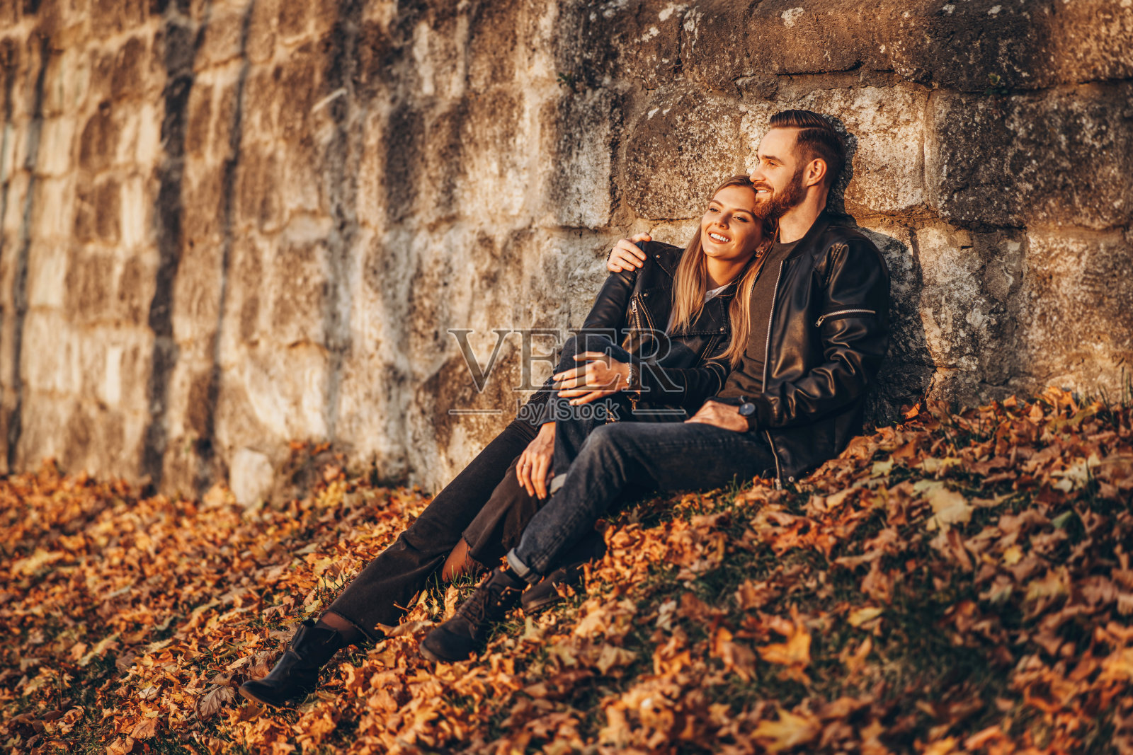 一对年轻的恋人坐在秋叶中,享受大自然照片摄影图片