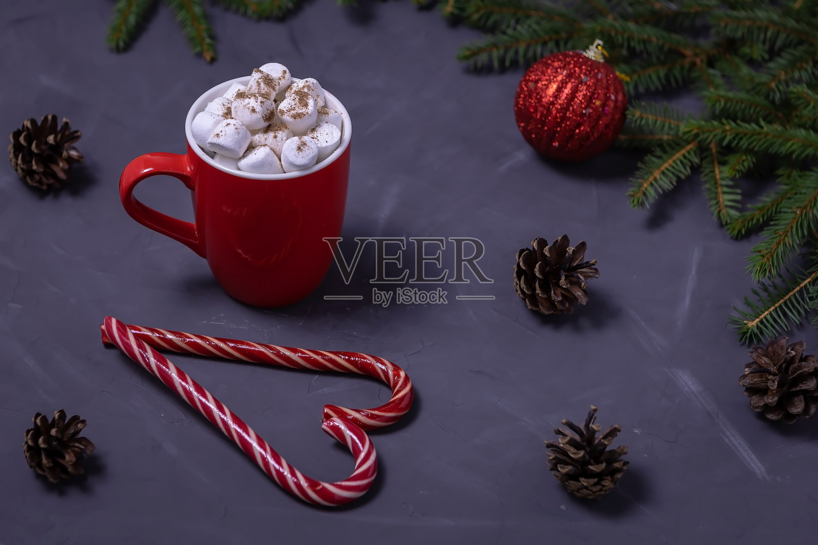 红色的杯子里有咖啡和棉花糖,圣诞糖果折叠成心形,一个球和在黑色背景上的冷杉树枝照片摄影图片