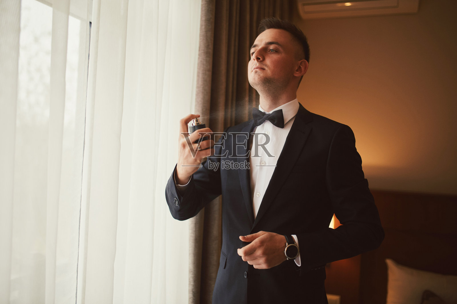 新郎在婚礼前的早晨。新郎早上准备。年轻英俊的新郎喷着香水。照片摄影图片