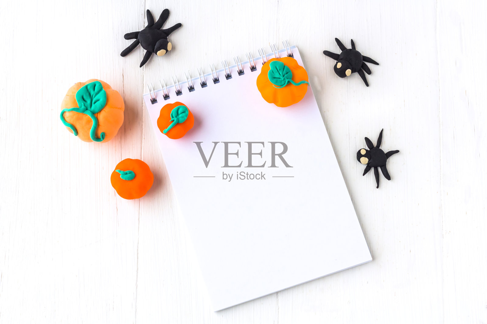 万圣节装饰:用塑料手工制作的南瓜和蜘蛛,白色木质背景上留有文字空间的笔记本。照片摄影图片