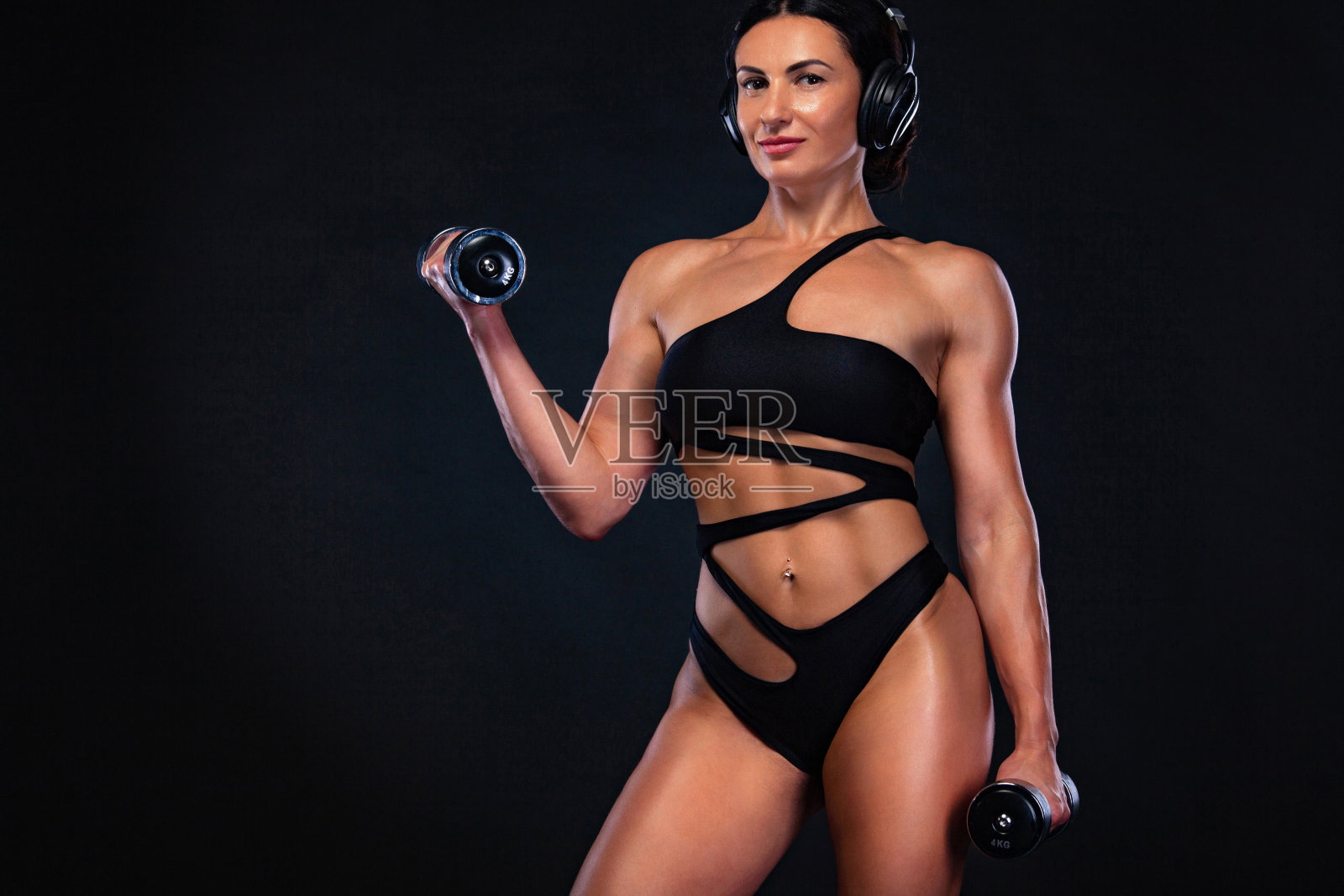 强壮的肌肉健美的女运动员用哑铃在黑色的背景上鼓起肌肉。锻炼健身的概念。照片摄影图片