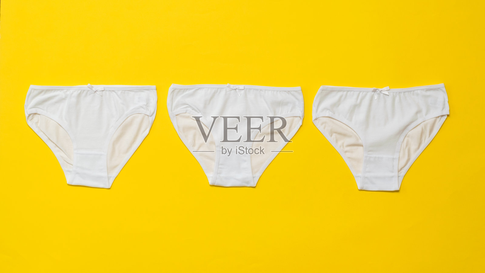 三条亮黄色背景上的白色女性内裤。平的。照片摄影图片