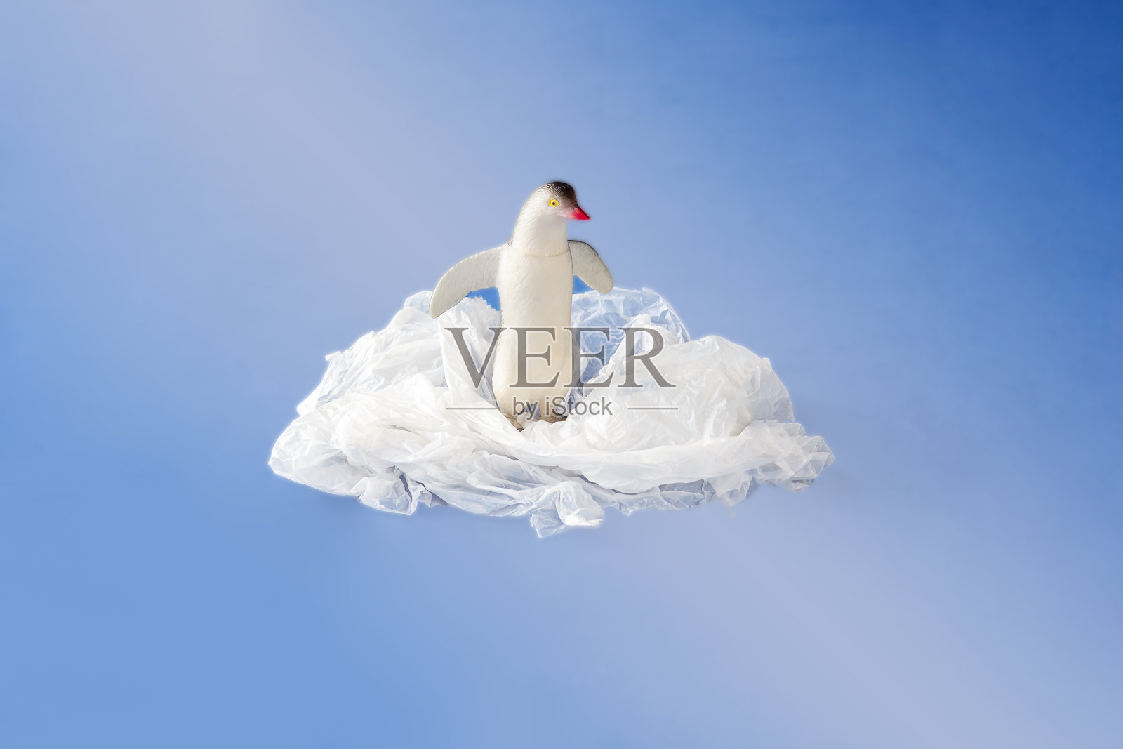 企鹅玩具纠缠在一个塑料袋在蓝色的背景。塑料污染的概念。环境问题。文本复制空间照片摄影图片