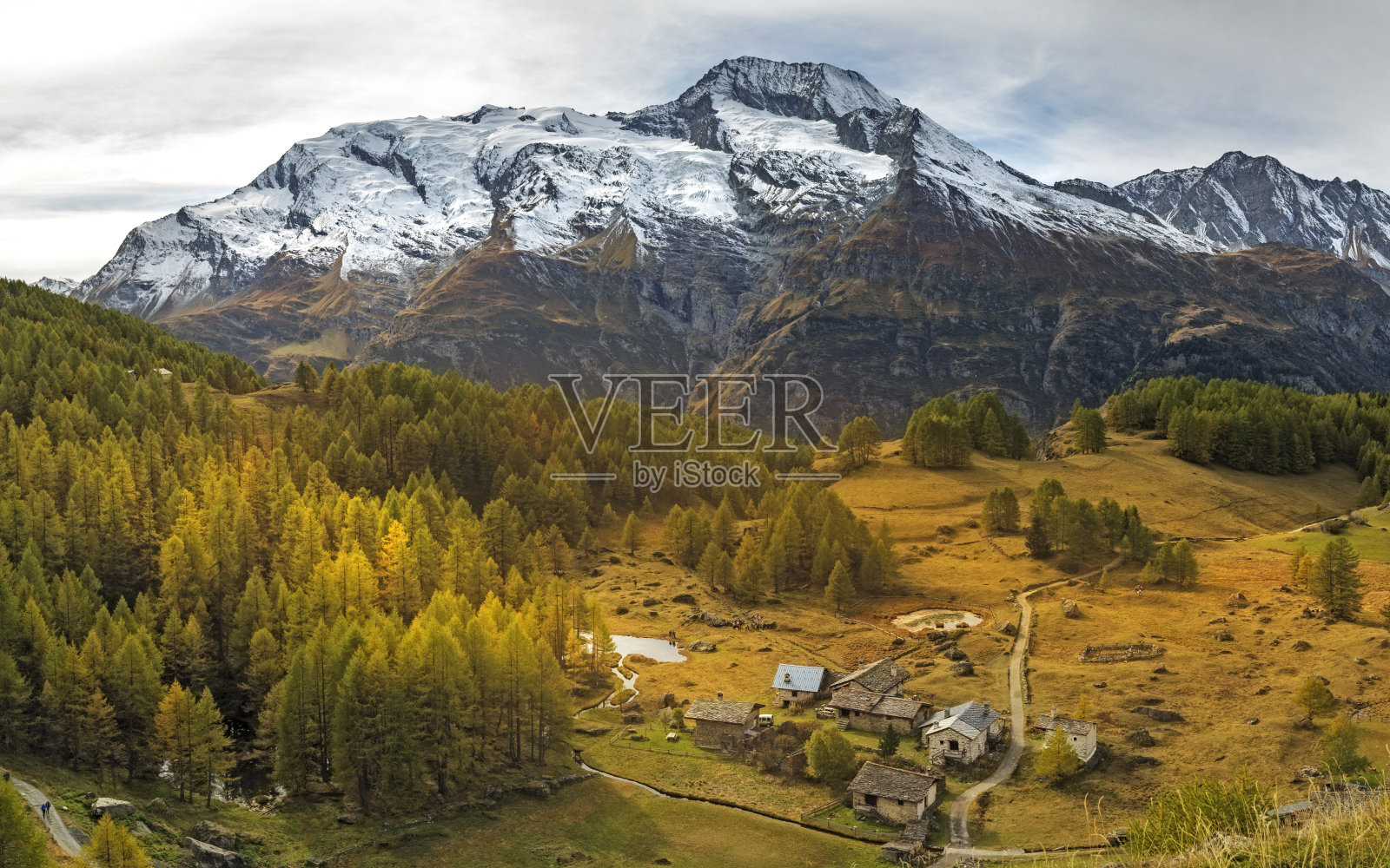 小山旁的小村庄,以白雪覆盖的高山为背景照片摄影图片