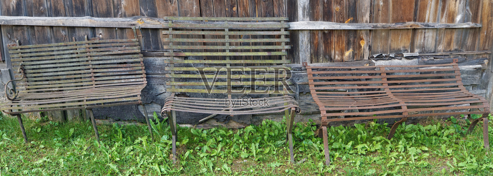 木栅栏旁有三张陈旧的生锈的公园长椅照片摄影图片