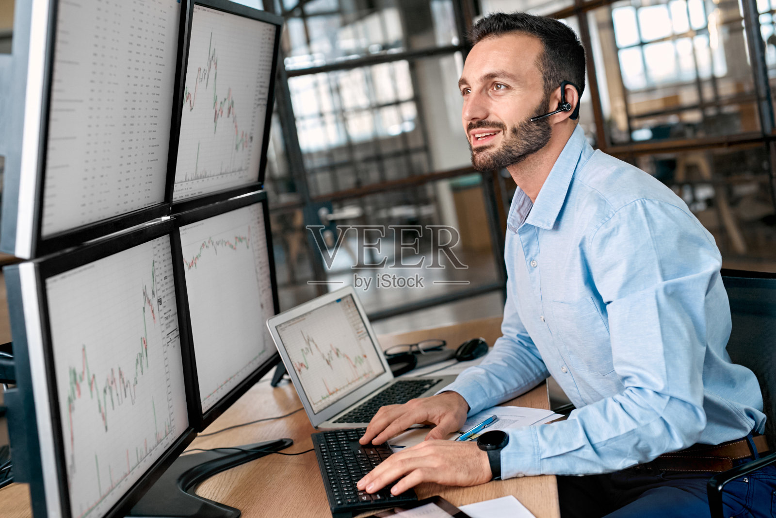 股票经纪人在电脑上查看加密货币信息,用耳机说话照片摄影图片