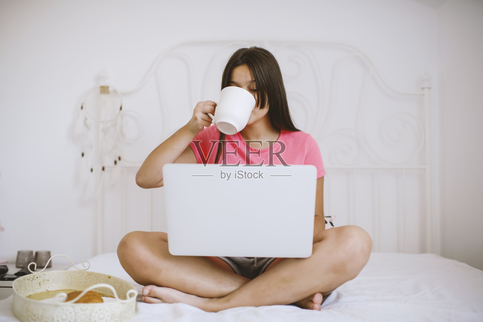 一个白人少女在床上吃健康早餐。她正在看笔记本电脑照片摄影图片