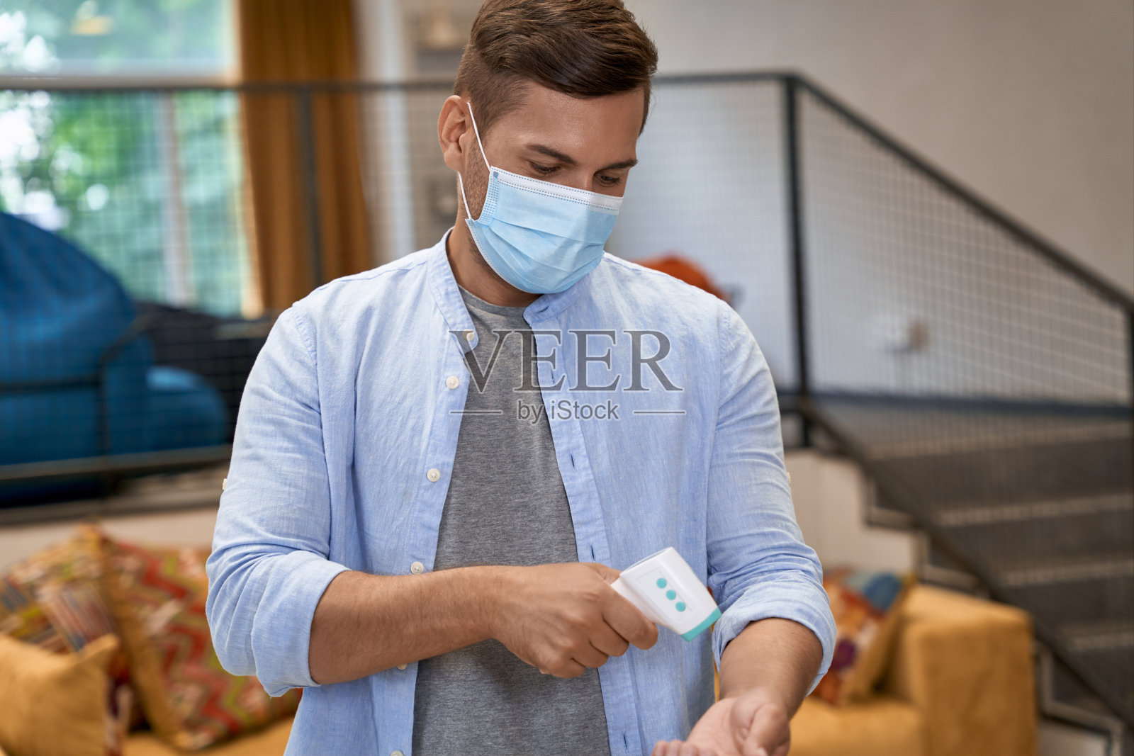 年轻男性上班族戴医用防护口罩站在办公室,用红外温度计测体温照片摄影图片