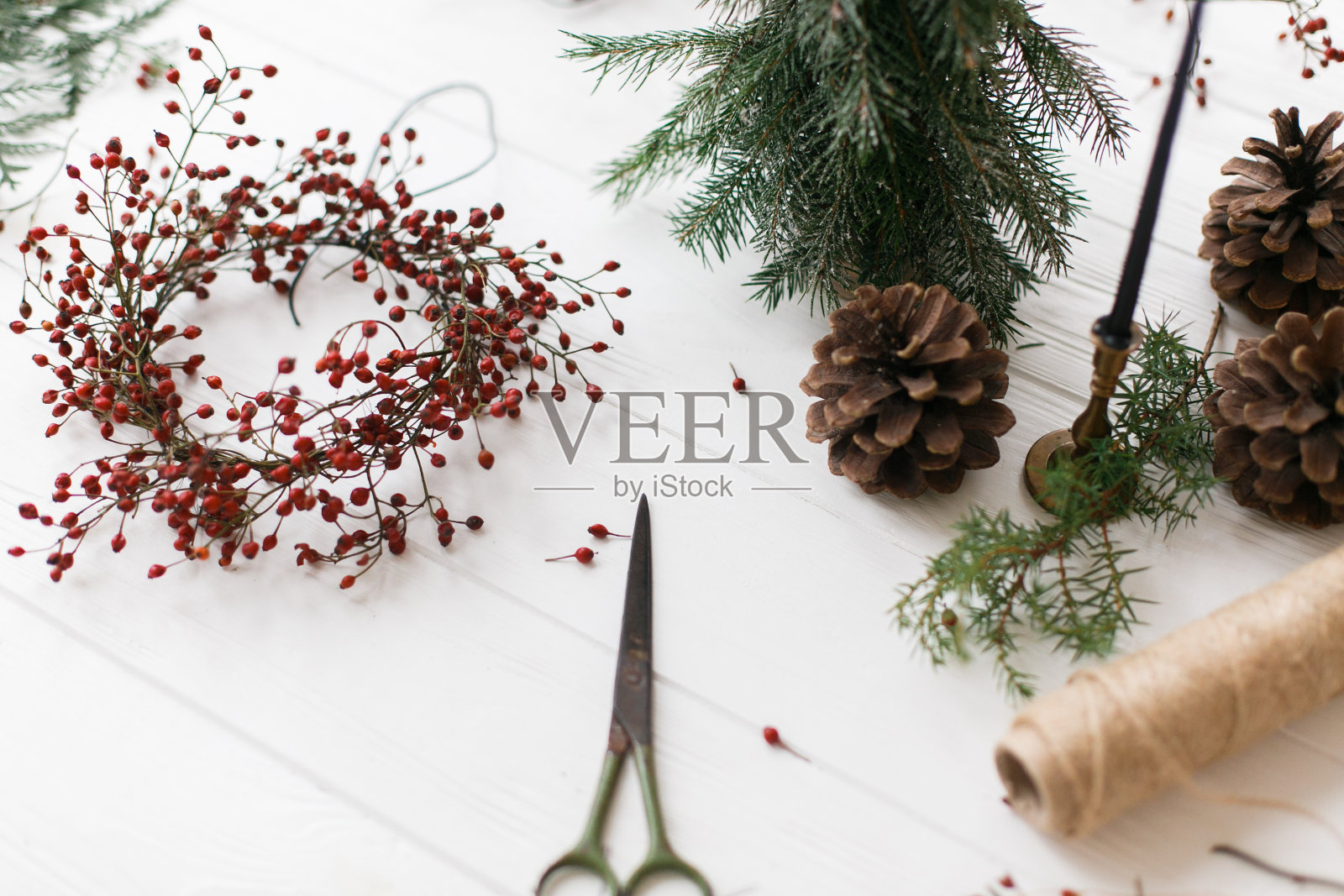 以红色浆果、线、剪刀、松果和蜡烛为背景装饰的圣诞花环照片摄影图片
