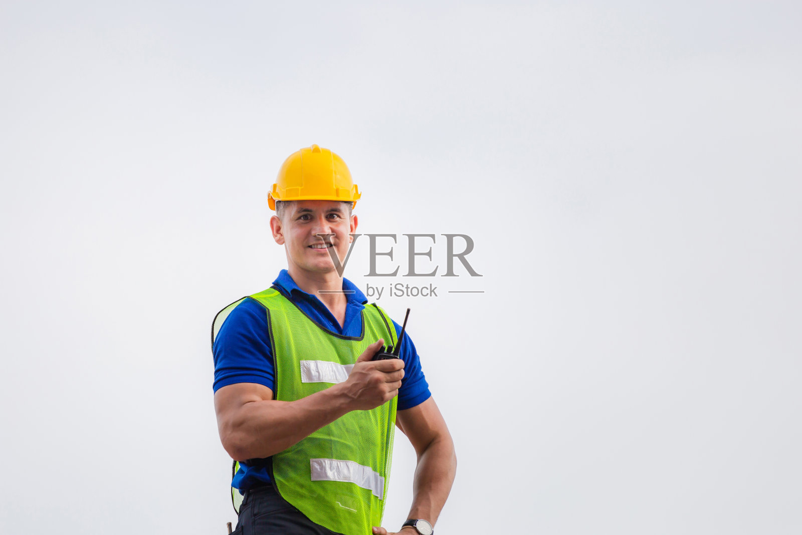 工头戴安全帽,穿着安全背心站在集装箱箱上,手持双向无线电控制器,看着摄像机照片摄影图片