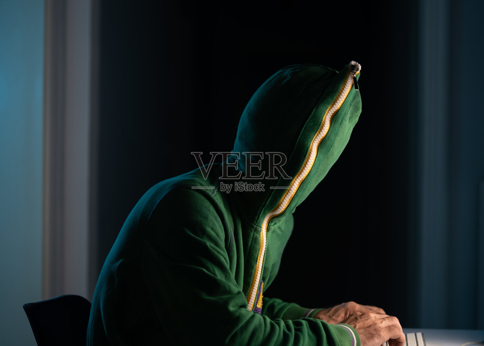 戴拉链帽衫和口罩的男子在黑暗中使用笔记本电脑进行黑客攻击照片摄影图片