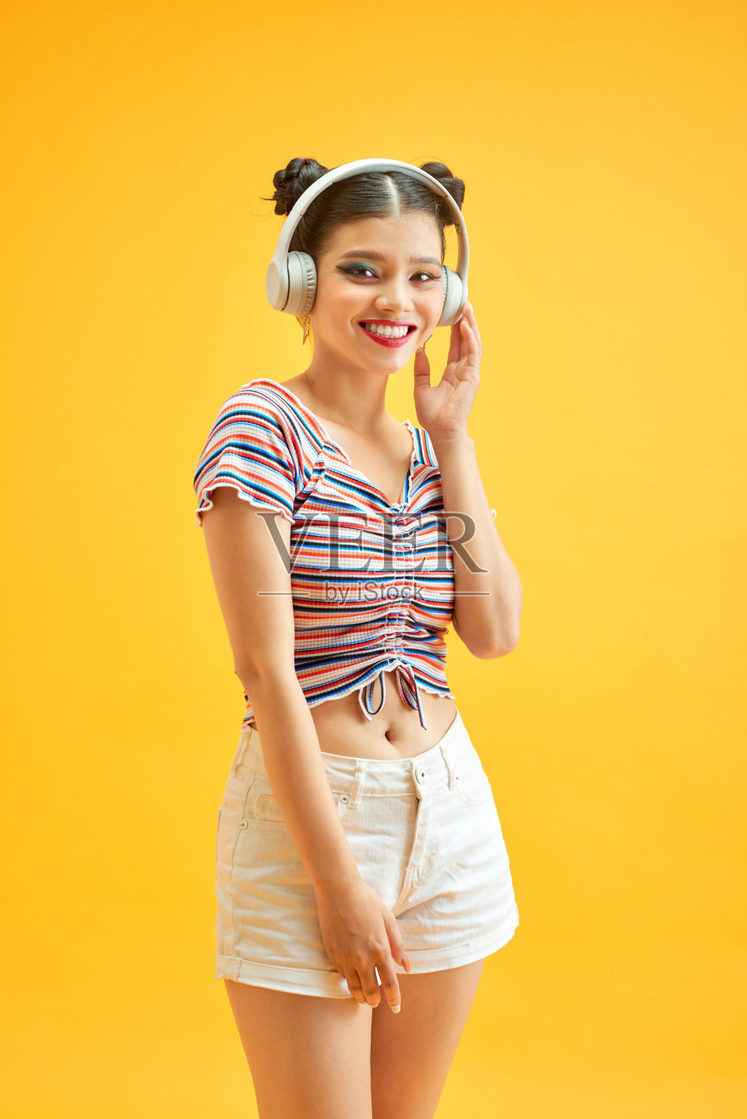 梳着发髻,戴着耳机听黄色背景音乐的年轻女士照片摄影图片
