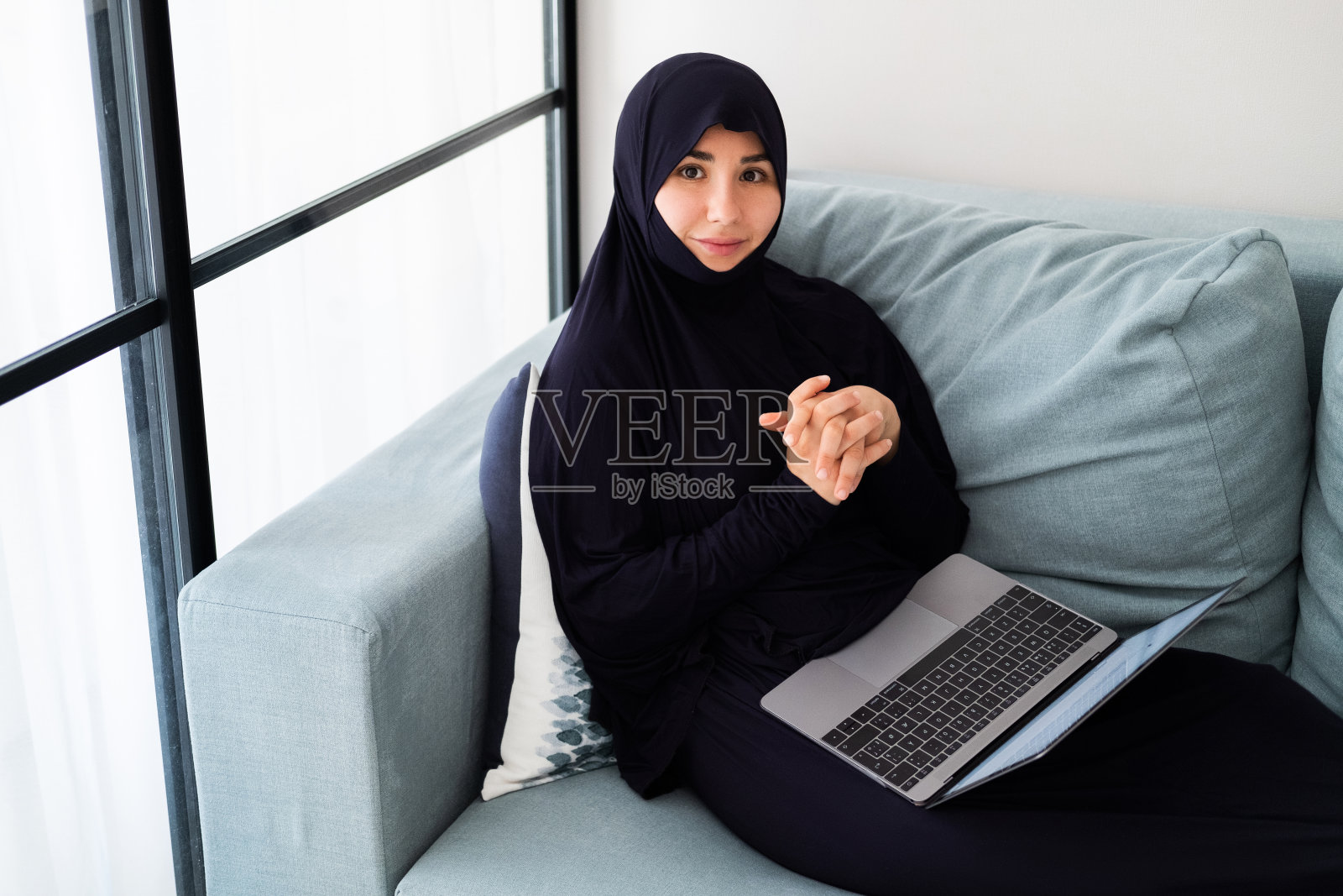 戴着头巾,在家用笔记本电脑工作的漂亮年轻穆斯林女孩照片摄影图片