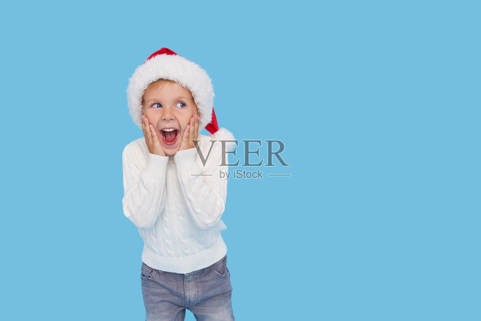 一个心满意足的小男孩戴着圣诞老人的帽子。笑声孤立在蓝色背景。哇的脸。折扣的季节照片摄影图片