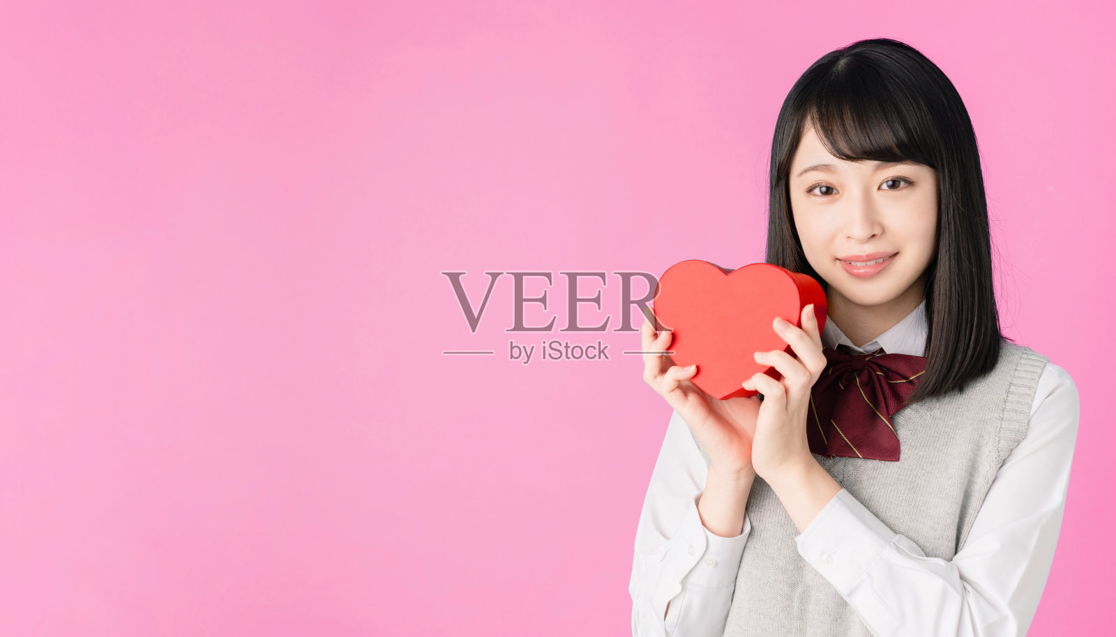 亚洲女学生拿着一个心形盒子。照片摄影图片