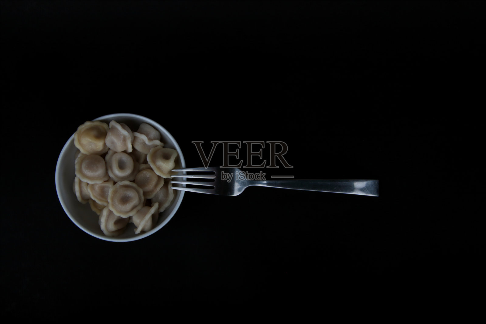 一碗白色的馄饨和一把叉子孤立地放在黑色的背景上照片摄影图片