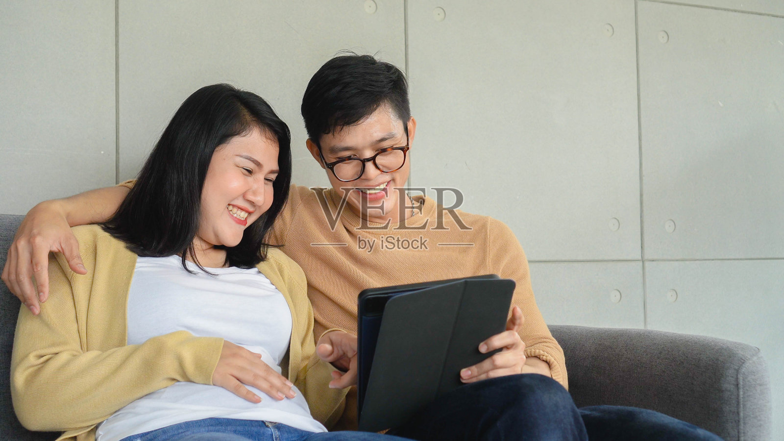 亚洲情侣情侣一起坐在沙发上,使用数字平板回顾超声胎儿结果从医学产科诊所为父母概念的开始快乐的感觉照片摄影图片