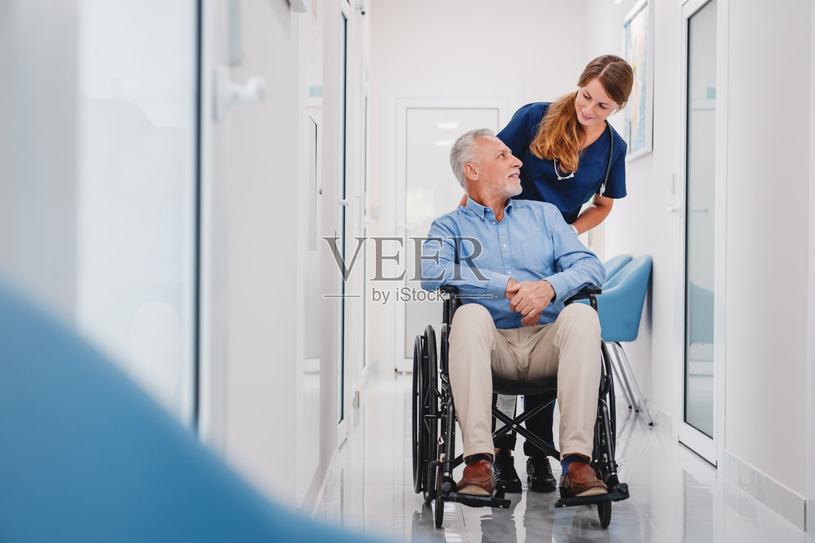 年长的男病人坐在轮椅上与女护士医生在医院走廊照片摄影图片