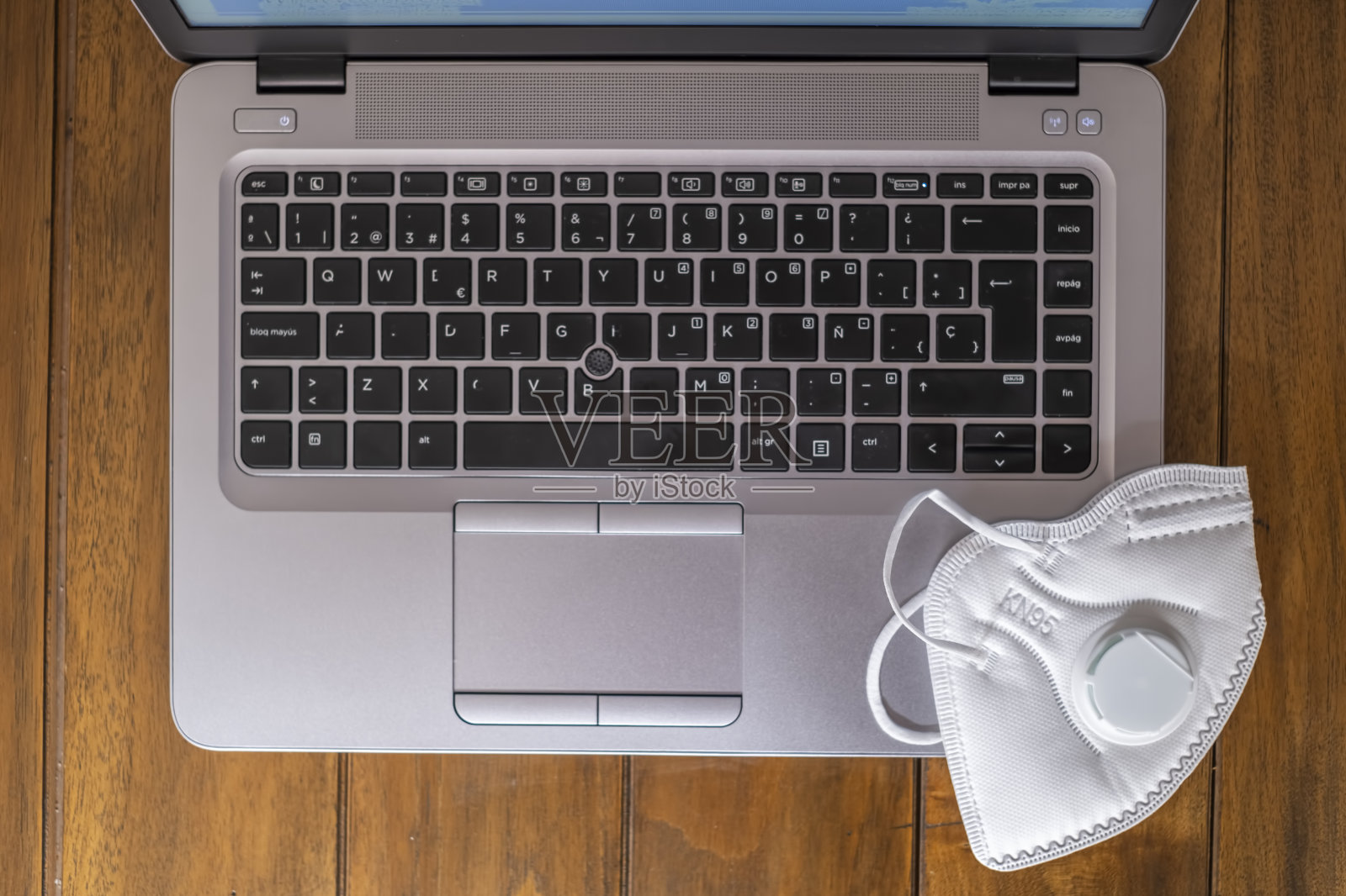 从上面看,笔记本键盘放在一张木制的桌子上,上面有一个白色的FPP2 KN95面罩照片摄影图片