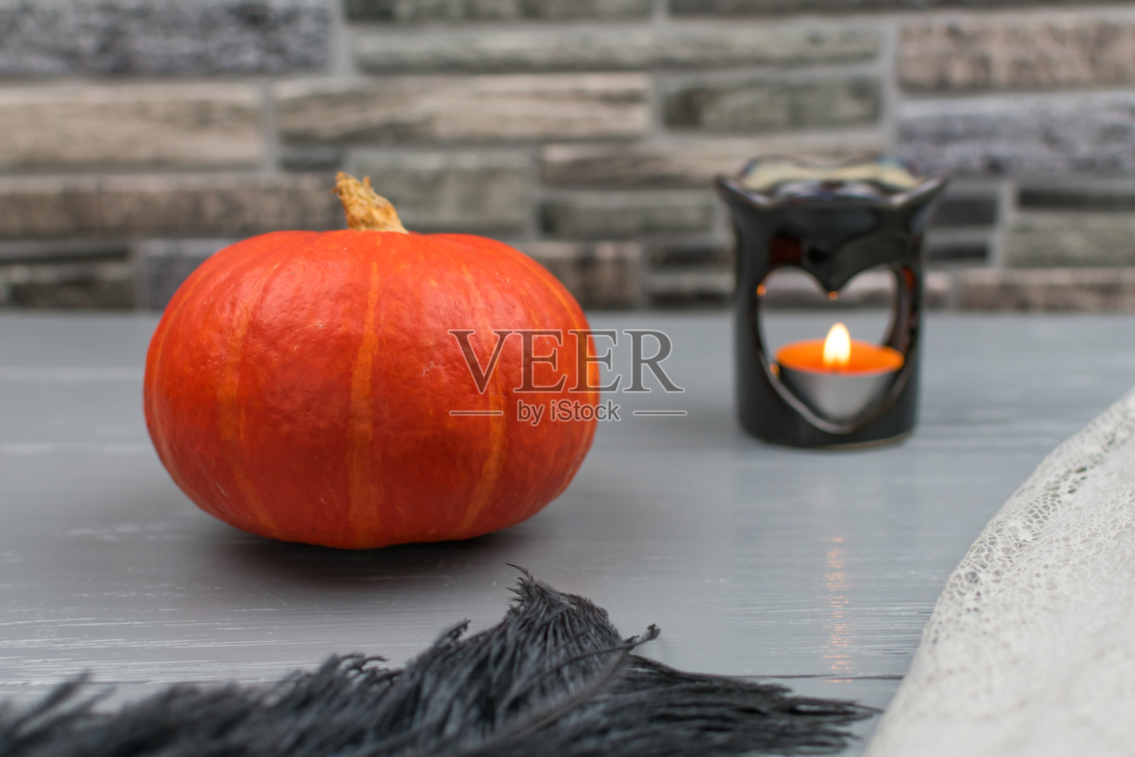 灰色木桌上放着黑色羽毛的橙色南瓜和心形香灯。有香味的蜡烛。秋天的概念,安慰。有选择性的重点。照片摄影图片