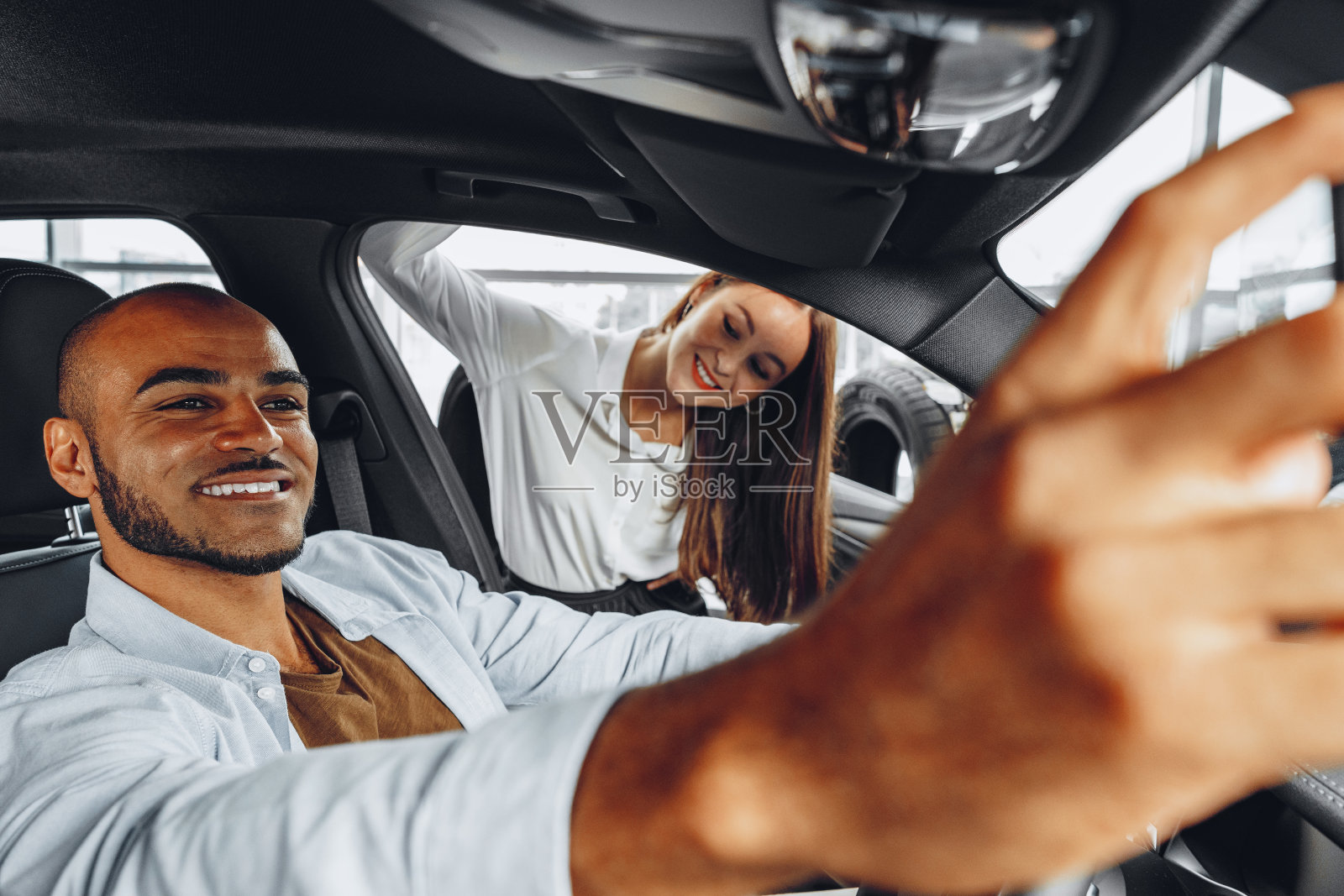 年轻迷人的女人销售员在汽车展厅展示一辆车给她的男性客户照片摄影图片