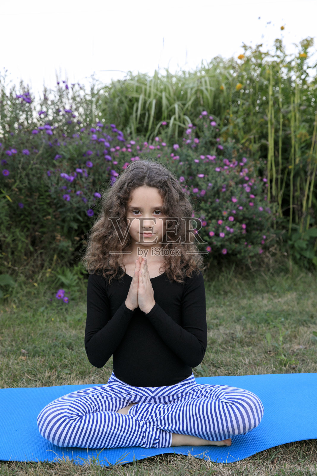 漂亮的小女孩坐在户外公园的垫子上练习冥想瑜伽。照片摄影图片