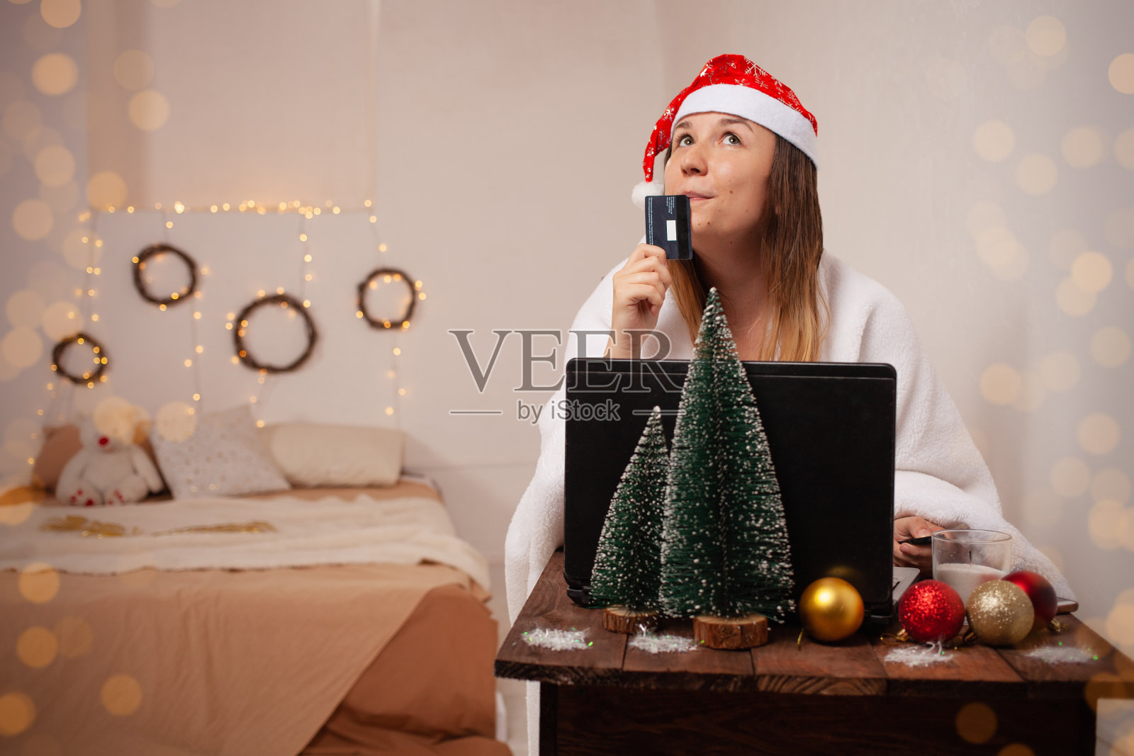 快乐的女人梦想着礼物和购物,在网上为圣诞节购物。新年内景,一个拿着信用卡的女孩坐在笔记本电脑前。网上订购节日礼物。照片摄影图片
